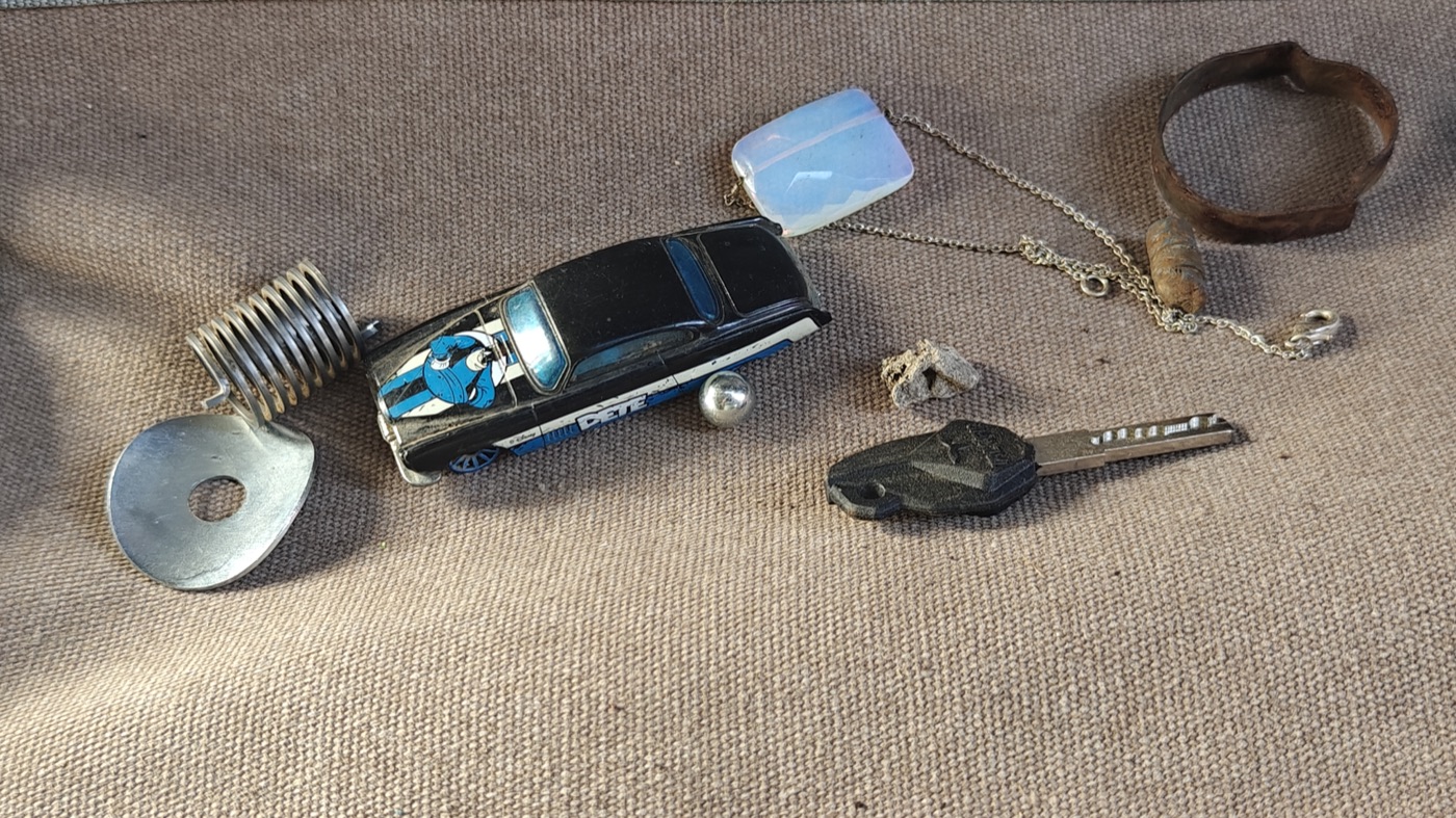 A small collection of found trinkets — a toy car, a pendant, an old ring, and other odds and ends