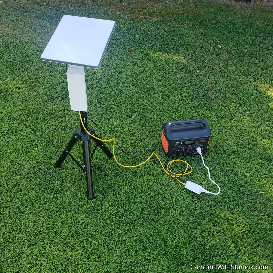 A tripod-mounted directional antenna wired to a portable power station on the lawn, testing the camping connectivity setup