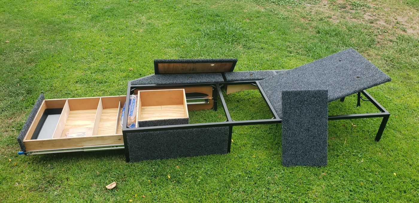 A homemade welded steel truck-bed platform with sliding wood drawers and carpeted panels
